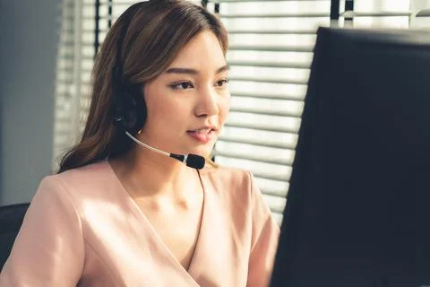 Competent female operator working on computer and while talking with clients. Foto stock