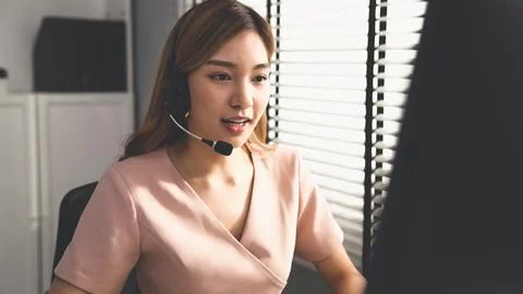 Competent female operator working on computer and while talking with clients. Foto stock