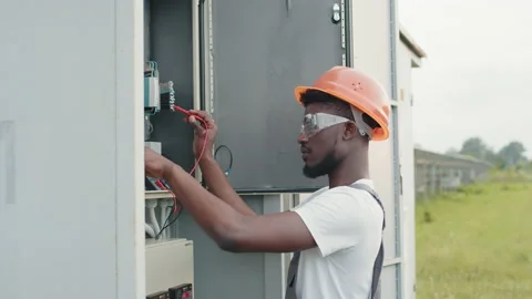 Competent technician in orange helmet and grey overalls standing near switchgear Stock Footage 168911029