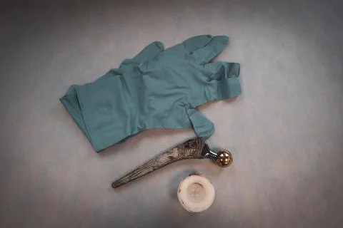 Complete explanted hip prosthesis lies on one hand with a blue medical glove Stock Photos