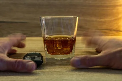 A completely drunk driver tries to pick up a glass of whiskey with ice from.. Stock Photos