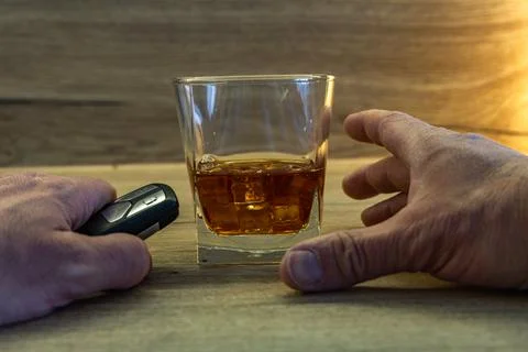 A completely drunk driver tries to pick up a glass of whiskey with ice from.. Stock Photos