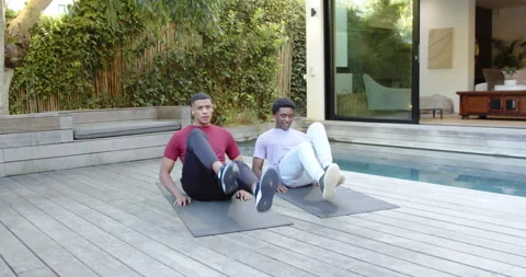 Completing flutter kicks on exercise mats, diverse male friends guiding Stock Footage 314027610