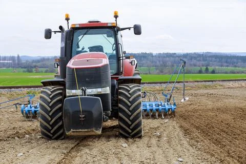 Complex of spring field works. A tractor with a seed drill in a field near the Stock Photos