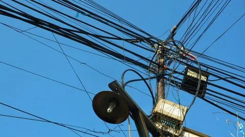 Complex tangle of power lines and cables on a utility pole against blue sky Stock Photos
