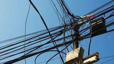 Complex tangle of power lines and cables on a utility pole against blue sky Stock Photos
