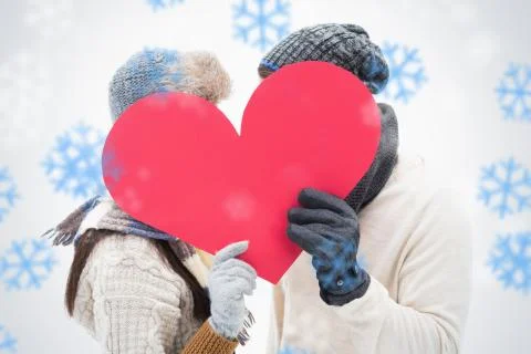 Composite image of attractive young couple in warm clothes holding red heart Illustrazione stock