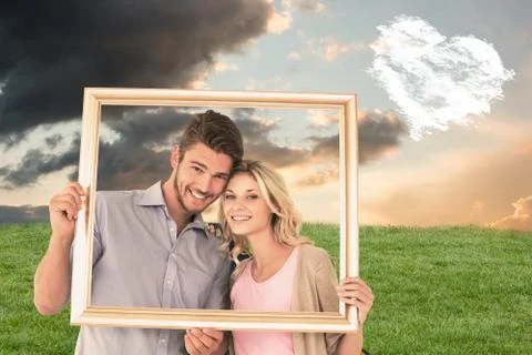 Composite image of attractive young couple holding picture frame Ilustração Stock