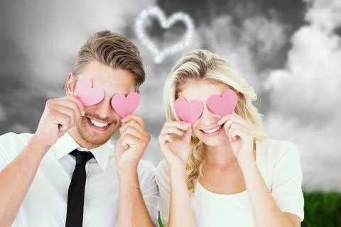 Composite image of attractive young couple holding pink hearts over eyes Ilustração Stock