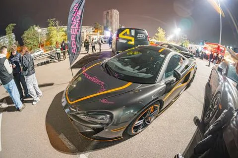 A composite image of a night scene at a car event, showing a luxury black spo Stock Photos
