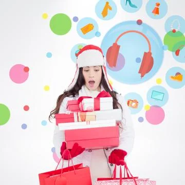 Composite image of surprised brunette in winter clothes holding many gifts and Stock Photos