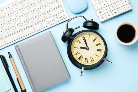 Composition with alarm clock, cup of coffee and computer keyboard on blue bac Stock Photos