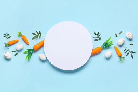 Composition with blank card, Easter eggs and green leaves on blue background Stock Photos