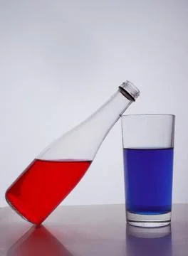 Composition from a bottle and glasses with multicolored liquid on a white bac Stock Photos