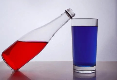 Composition from a bottle and glasses with multicolored liquid on a white bac Stock Photos