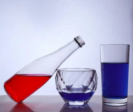 Composition from a bottle and glasses with multicolored liquid on a white bac Stock-Fotos
