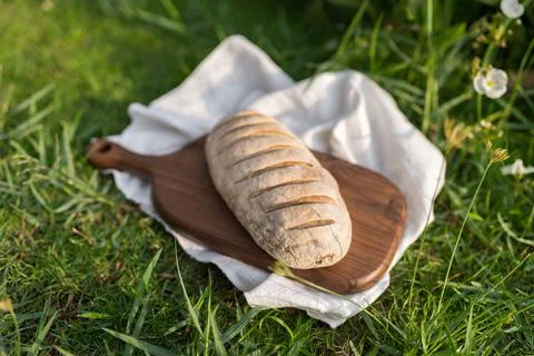 Composition of bread on wood board with white cloth napkin on the grass Stock Photos