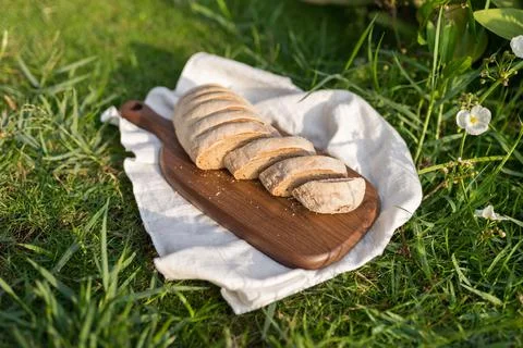 Composition of bread on wood board with white cloth napkin on the grass Stock Photos