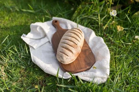 Composition of bread on wood board with white cloth napkin on the grass Stock Photos