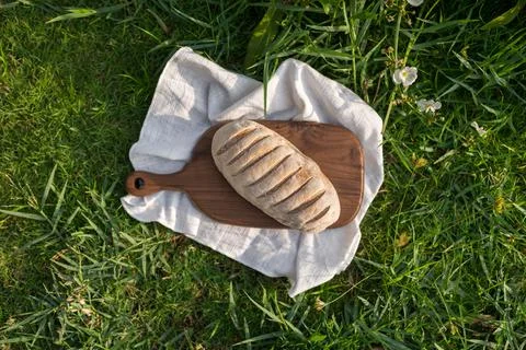 Composition of bread on wood board with white cloth napkin on the grass Stock Photos