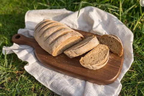 Composition of bread on wood board with white cloth napkin on the grass Stock Photos