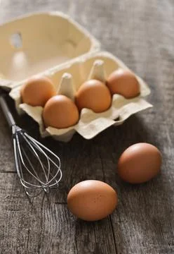 Composition with brown eggs and whisk on the old rustic backgrou Stock Photos
