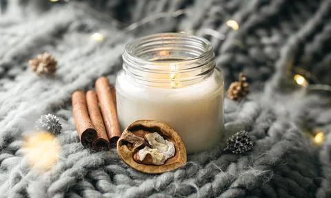 Composition with burning candle and cinnamon sticks on a knitted background. Stock Photos