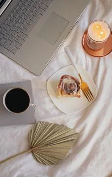Composition with cinnamon bun, coffee, burning candle and laptop on the bed. Stock Photos