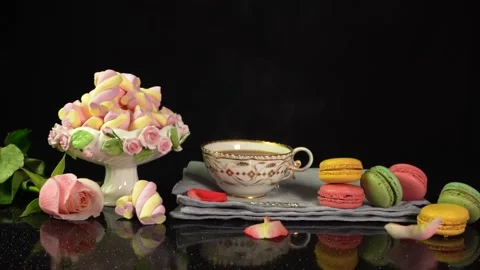 Composition with a cup of tea, macaroons, marshmallows and falling rose petals Stock Footage 147874981