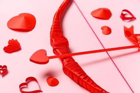 Composition with cupid's bow and paper hearts on pink background, closeup. Va Stock Photos