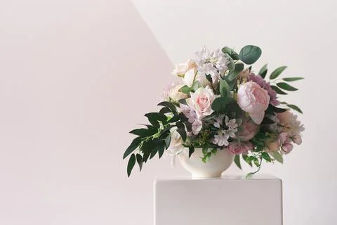 A composition of different flowers in a white vase on a square podium. The Stock Photos