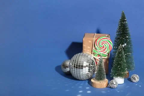 Composition with disco balls, Christmas trees and gift box on blue background Stock Photos