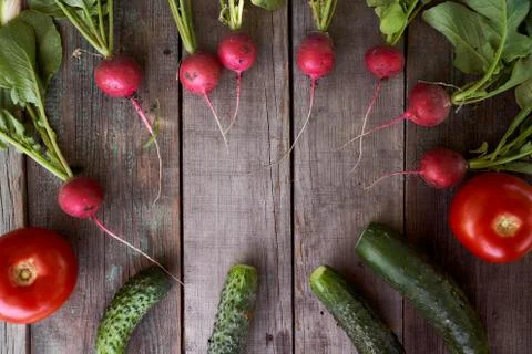Composition Fresh radish with bots and cucumbers rests on old wooden boards.  Stock Photos