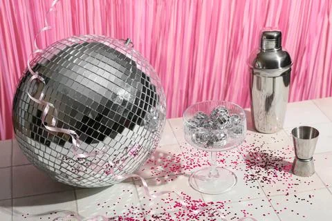 Composition with glass, bartender tools and disco balls on white tile table n Stock Photos