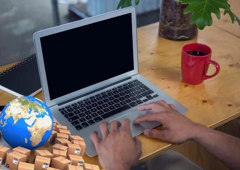 Composition of globe with cardboard boxes over man using laptop 写真素材