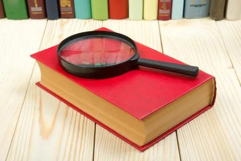 Composition with hardback book and magnifying glass on the table. Back to school Stock Photos