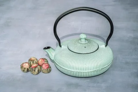Composition with Iron teapot and aromatic green tea flowers ball on gray Stock Photos