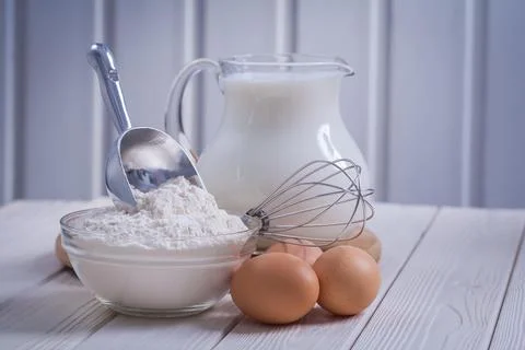 Composition of kitchen objects eggs corolla bowl with flour jug milk on white Stock Photos