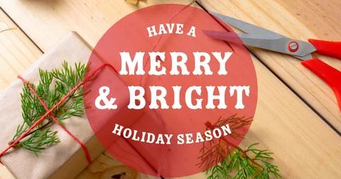 Composition of merry and bright text over present and scissors on table at Stock Illustration