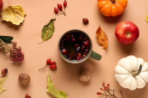 Composition with mug of hot berry tea, pumpkins and autumn decor on beige bac Stock Photos