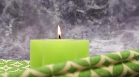 Composition with one green lit candle on a table with a green linen napkin .. Stock Photos
