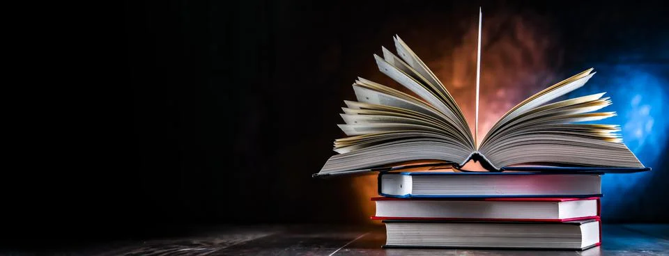 A composition with an open book lying on a stack of other books 스톡 사진