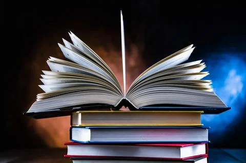 A composition with an open book lying on a stack of other books Stock Photos