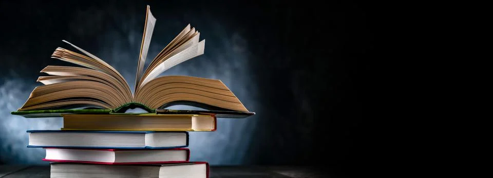 A composition with an open book lying on a stack of other books 写真素材