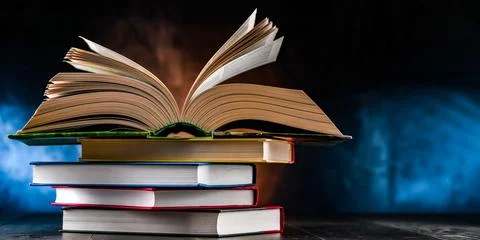 A composition with an open book lying on a stack of other books Stock Photos