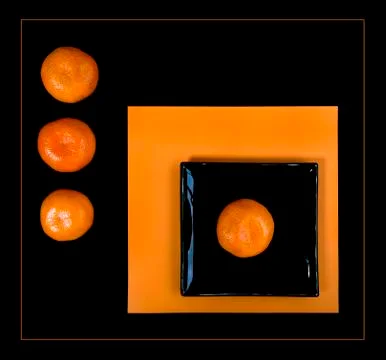 Composition of orange mandarin and black square plate on an orange table. Stock Photos