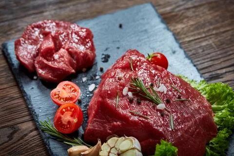 Composition of raw beefsteak on slate board with vegetables and seasoning Stock Photos