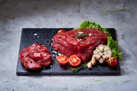 Composition of raw beefsteak on slate board with vegetables and seasoning Stock Photos