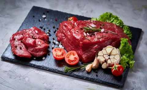 Composition of raw beefsteak on slate board with vegetables and seasoning Stock Photos