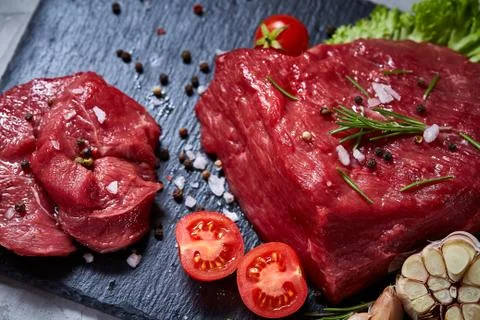 Composition of raw beefsteak on slate board with vegetables and seasoning Stock Photos